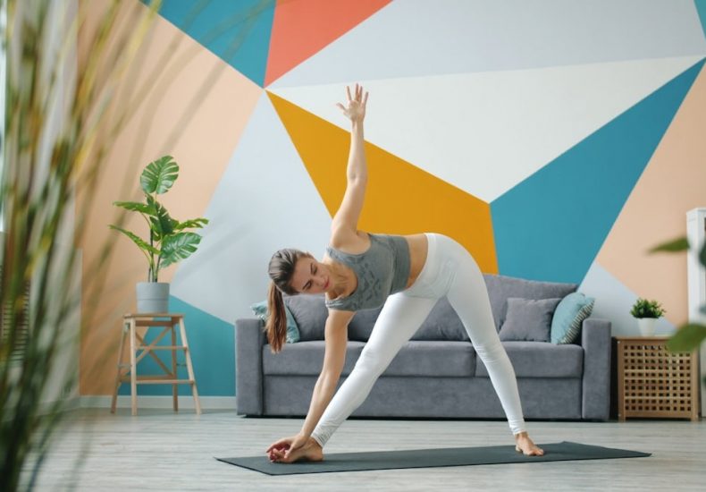 Portrait of cute lady in leggings and top doing yoga at home working out standing on mat exercising. Healthy youth lifestyle and indoor activities concept.